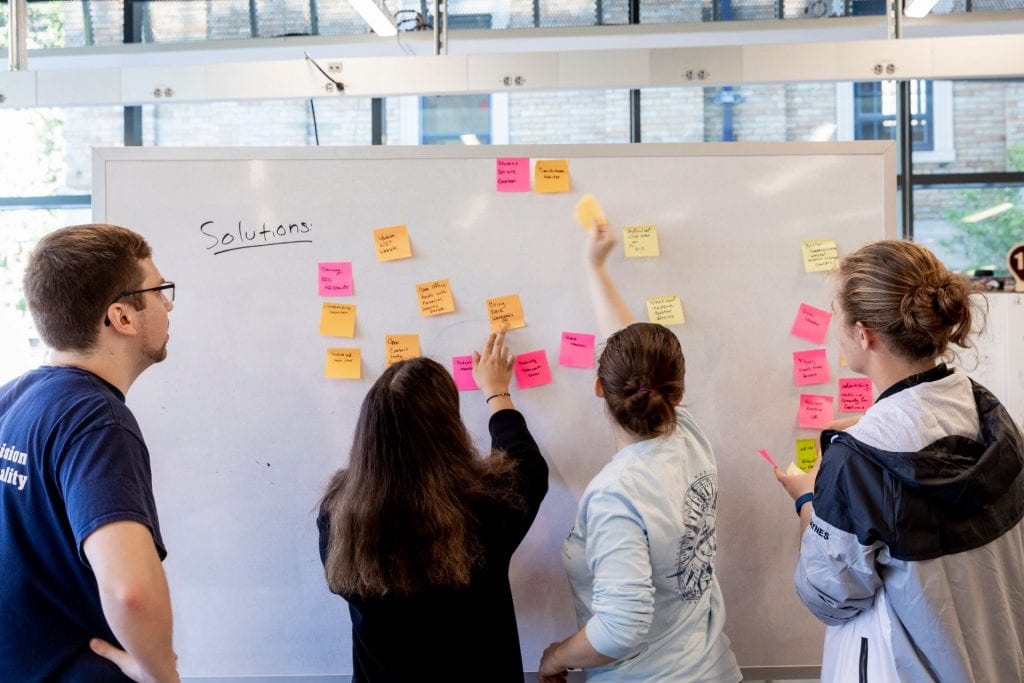 students placing sticky notes on a whiteboard 