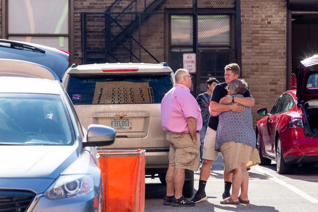 two parents hug their son in a parking lot