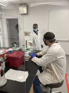 two people wearing lab coats and facemasks